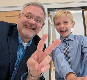 Gregory Mattingly smiling and making a peace sign beside a smiling child